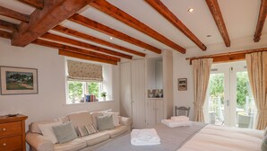 A cozy bedroom with a bed, a sofa, a dresser, and a window with curtains. - Glen View Cottage (Ambleside)