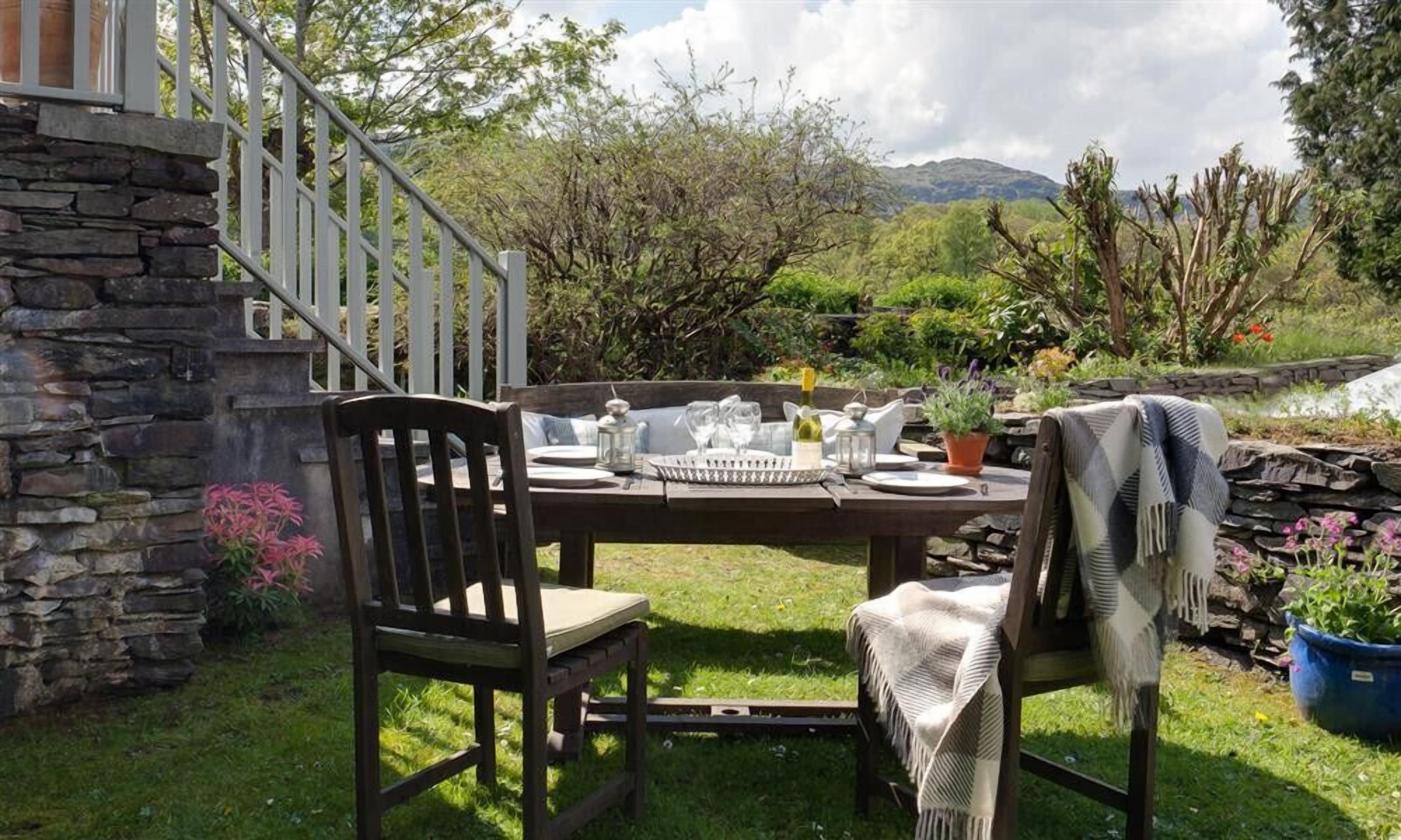 An outdoor dining area with a stone wall, a wooden table set for two, and a view of the surrounding landscape.