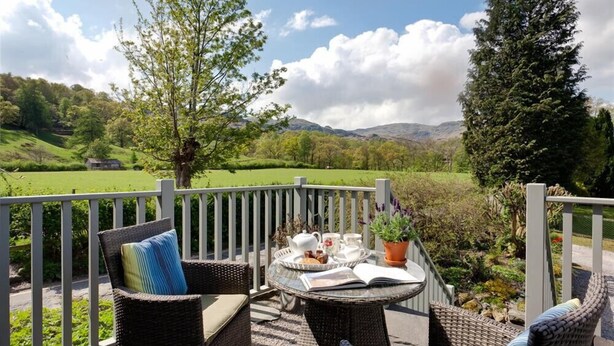 A balcony with wicker furniture, a table with a book, a teapot, and a tray with pastries. - Glen View Cottage (Ambleside)