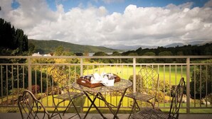 A balcony with a table and chairs overlooking a green landscape with hills and a lake. - Harrison Stickle (Windermere)