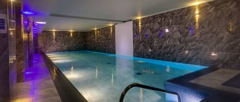 A modern indoor swimming pool with stone walls and ambient lighting.