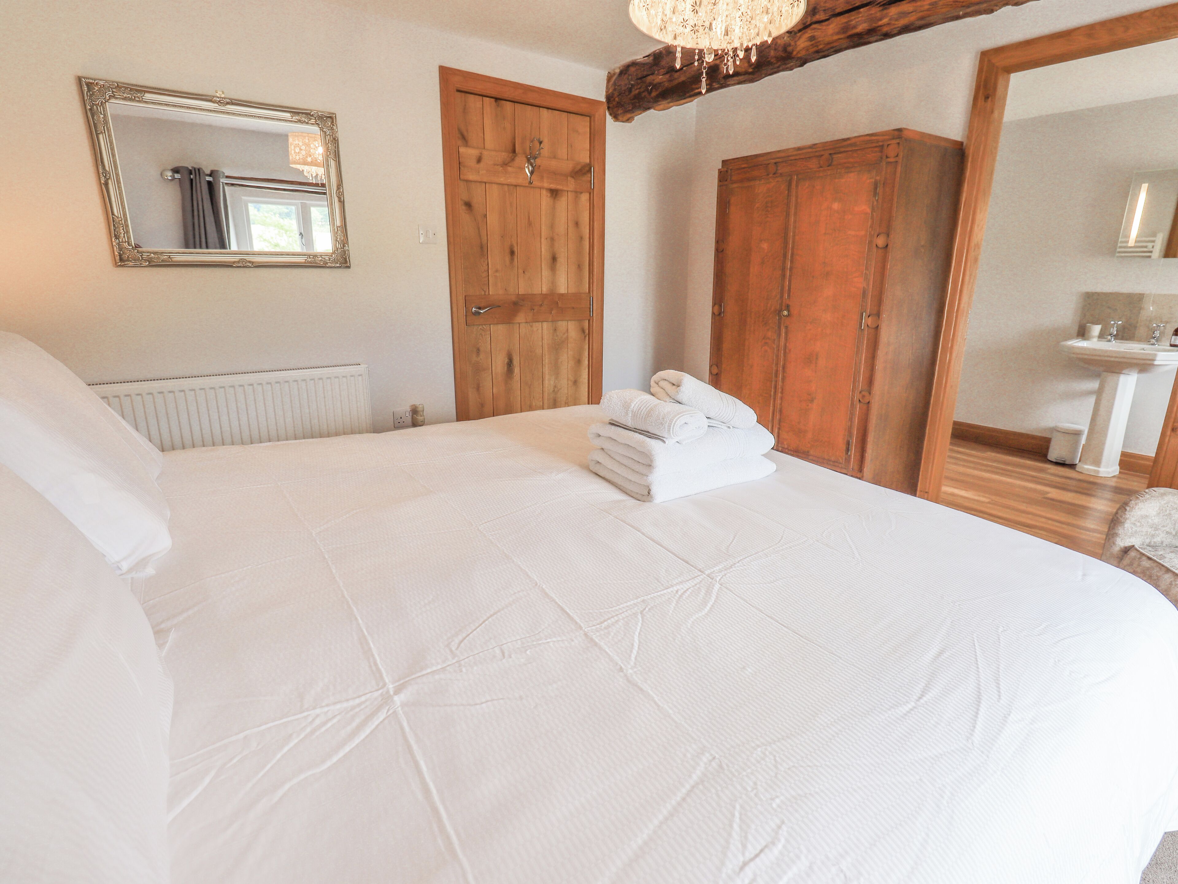 A bedroom with a large bed, wooden wardrobe, and a mirror.