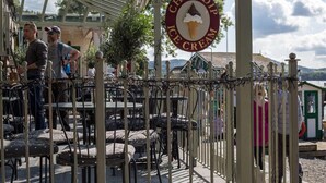 An outdoor seating area with tables and chairs, a sign for 'Choc Dip Ice Cream', and a fenced area with a person standing by. - Waterside (Ambleside)