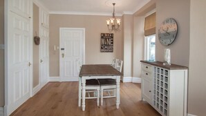 A dining area with a wooden table and chairs, a chandelier, a clock, and a cabinet with drawers. - Waterside (Ambleside)