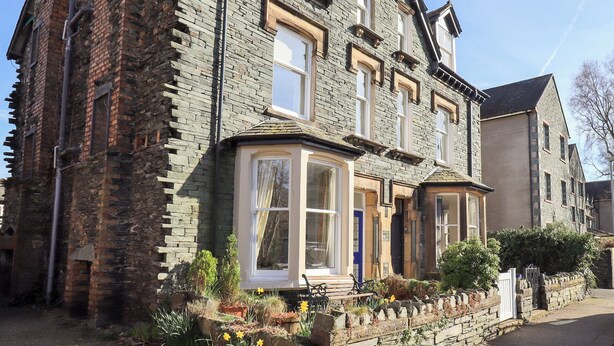 A two-story stone house with a bay window, a front door, and a small garden with flowers. - Number Twenty (Keswick)