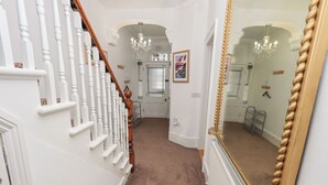 A hallway with white walls, a brown carpet, a wooden staircase, and a large mirror. - Number Twenty (Keswick)