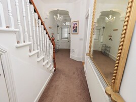 A hallway with white walls, a brown carpet, a wooden staircase, and a large mirror.