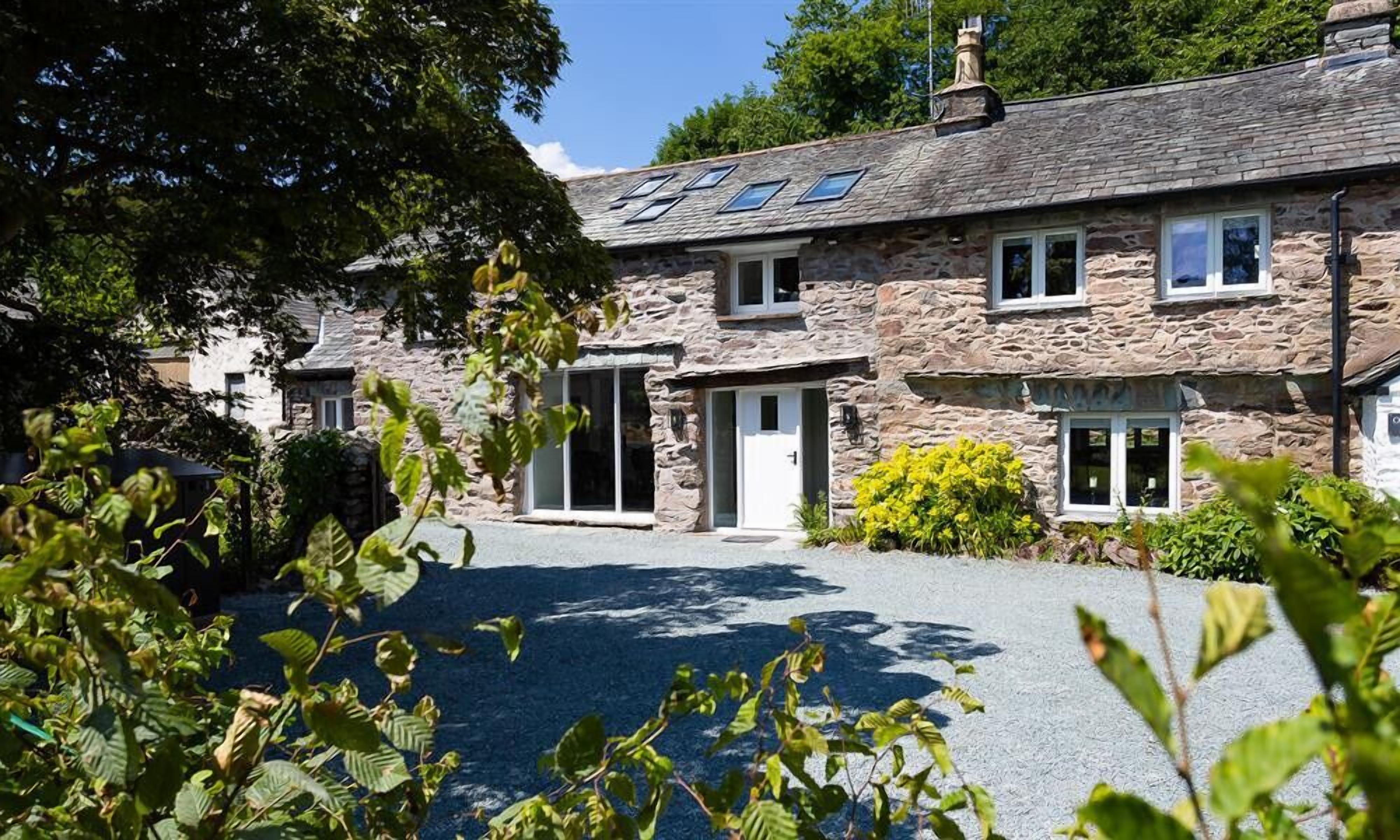 A stone building with a sloped roof, multiple windows, and a paved driveway.