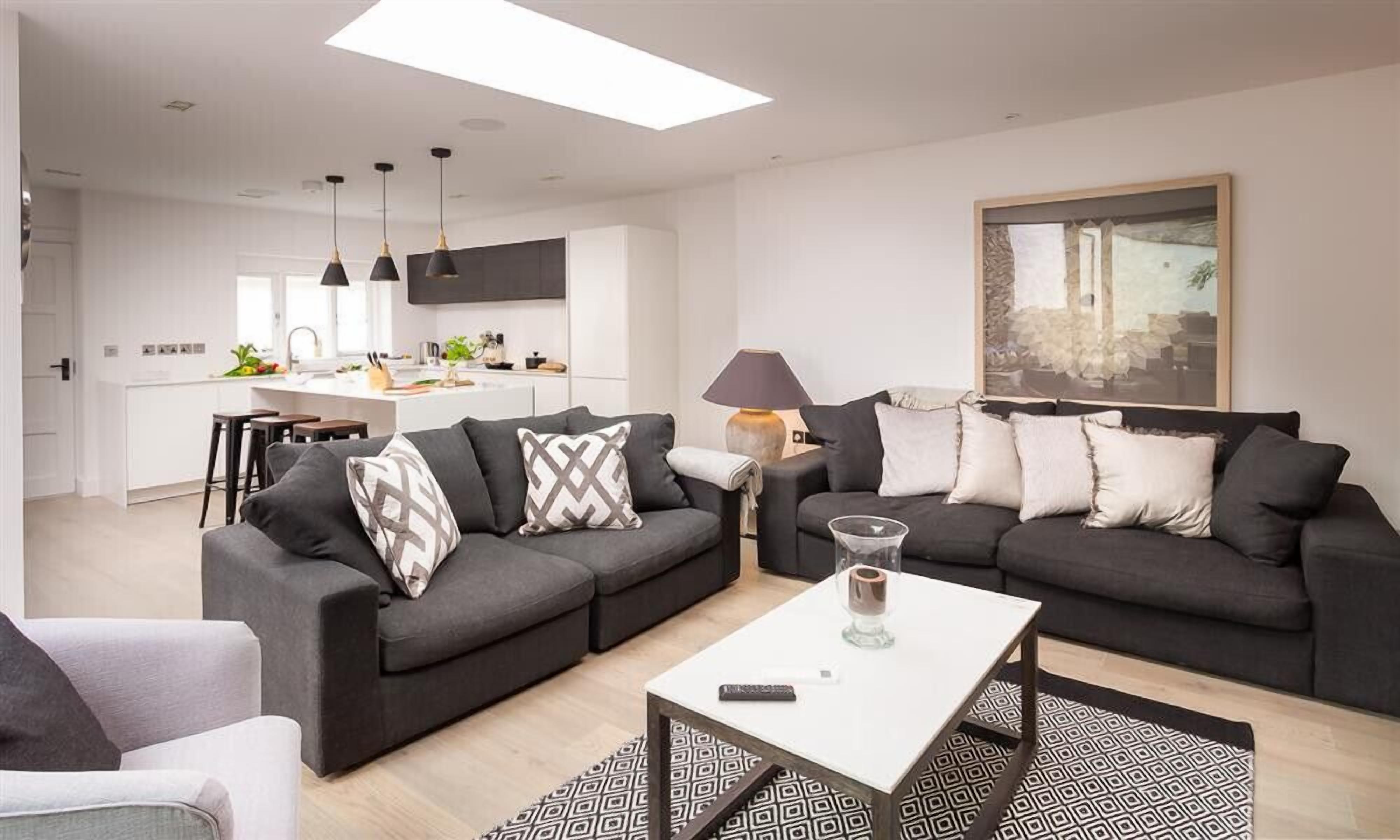 Una sala de estar moderna con un sofá gris, una mesita de centro y una cocina al fondo.