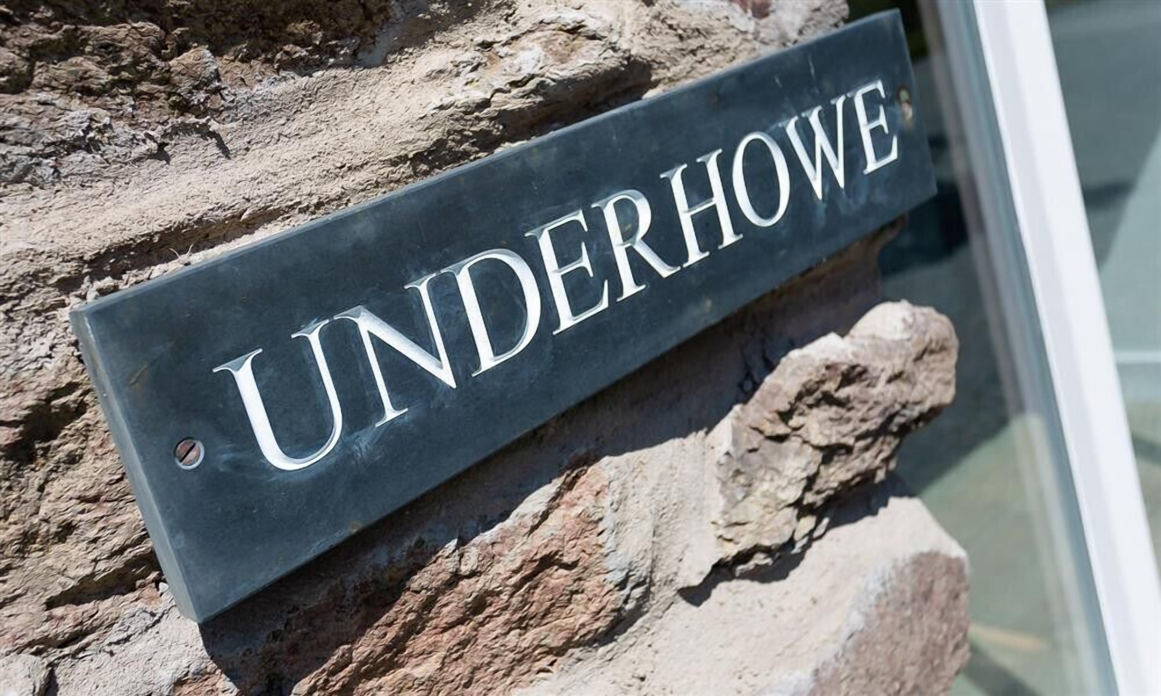 A sign with the name "UNDERHOWE" mounted on a stone wall.