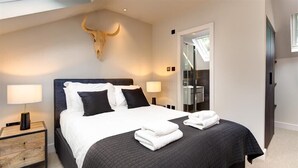 Une chambre moderne avec un grand lit, deux tables de chevet, une décoration murale représentant une tête de taureau et une vue sur la salle de bain à travers une porte en verre.