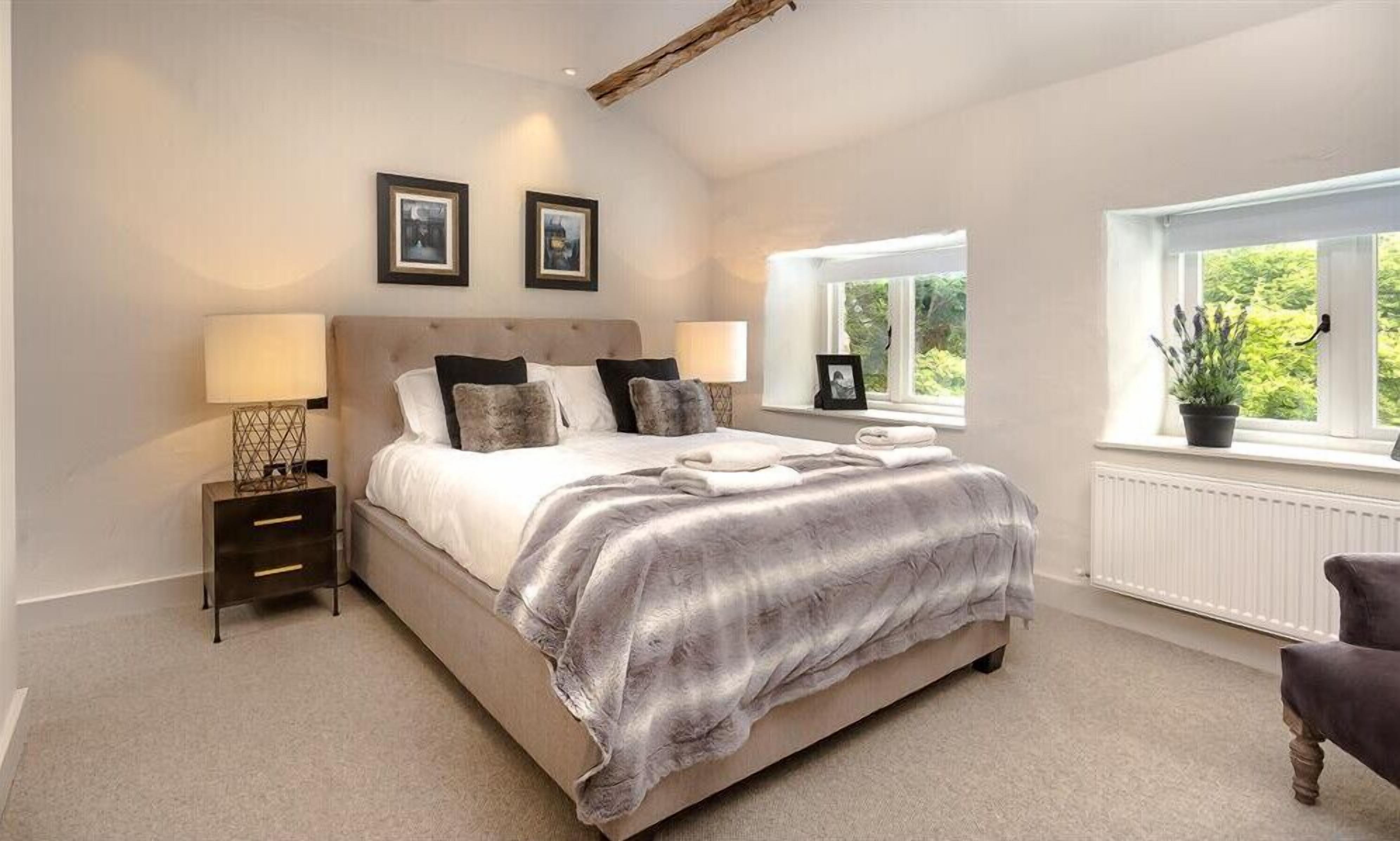 A bedroom with a large bed, two bedside lamps, a nightstand, a window with a view of greenery, and a potted plant on the windowsill.
