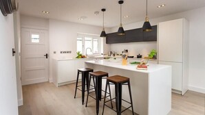 Une cuisine moderne dotée d’un îlot central, de tabourets de bar, de luminaires suspendus et d’une grande fenêtre.