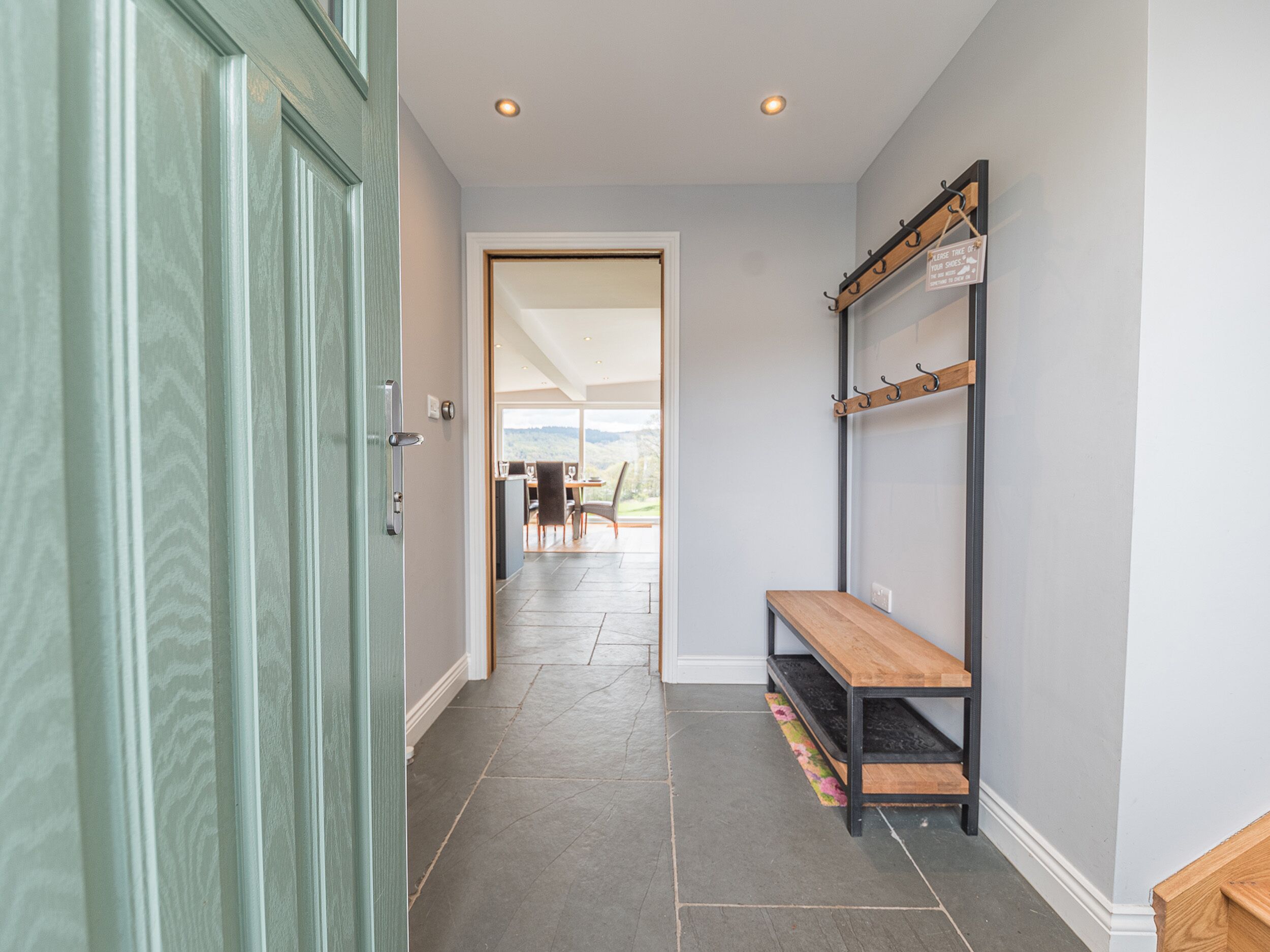 A hallway with a wooden bench, a coat rack, and a door leading to a dining area with a view.