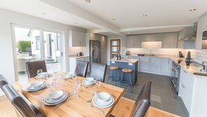 Een moderne keuken met grijze kastjes, een houten eettafel gedekt voor zes personen en een groot kookeiland met barstoelen.