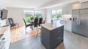 Een moderne keuken met een groot eiland, donkere kastjes en uitzicht op een tuin door de schuifdeuren.