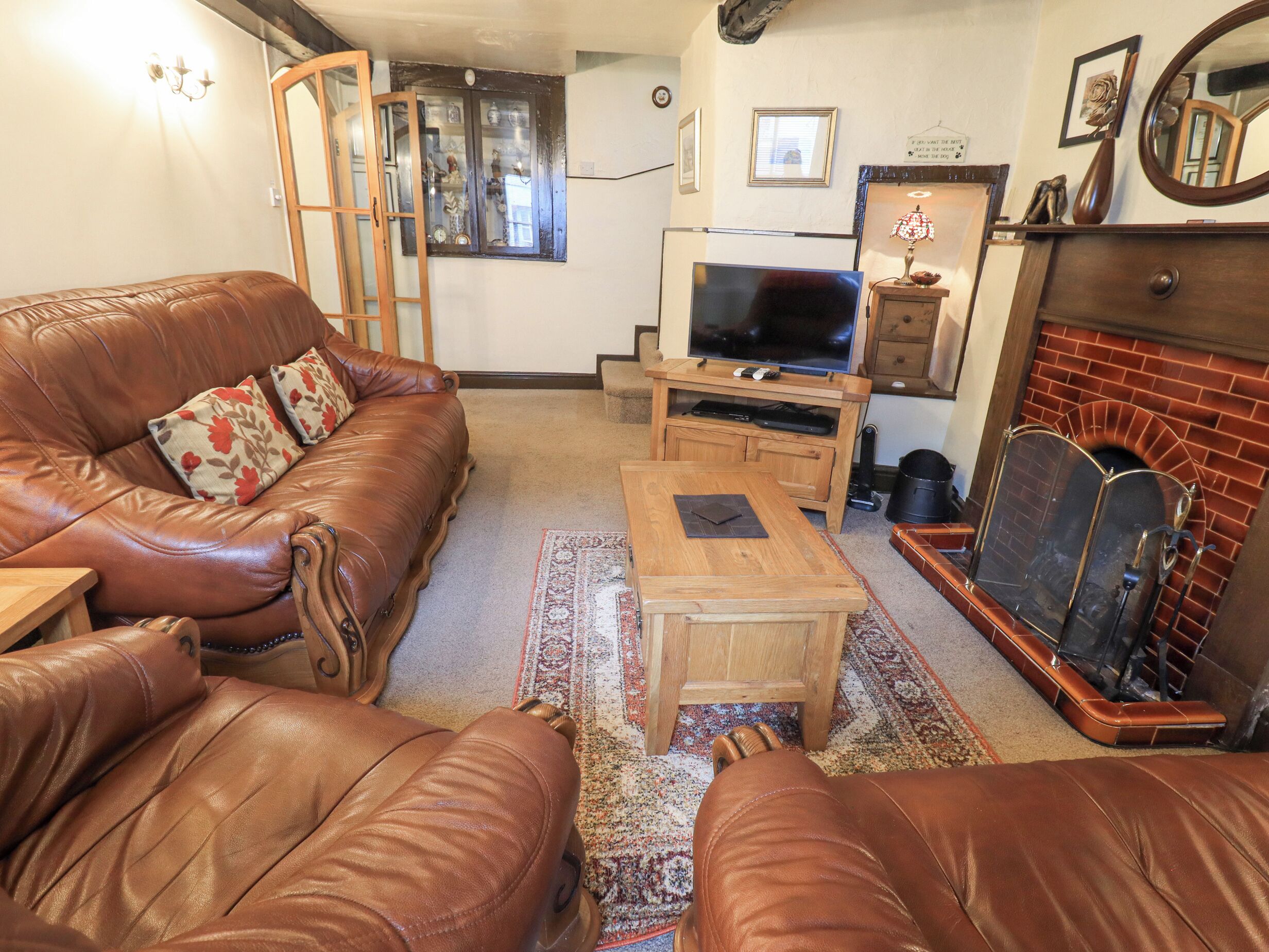 Ein Wohnzimmer mit einer Ledersofa, einem Holztisch, einem Fernseher auf einem Holzständer, einem Kamin und einem gemusterten Teppich.