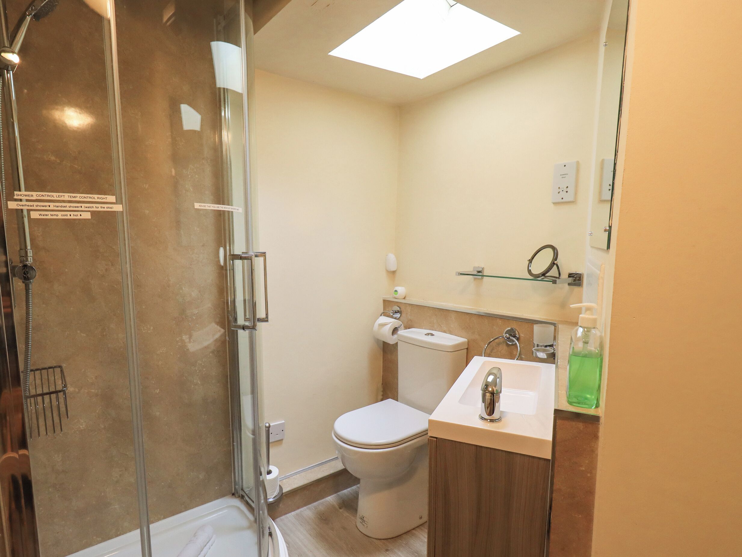 Un baño moderno con ducha de vidrio, inodoro y lavamanos con espejo arriba.