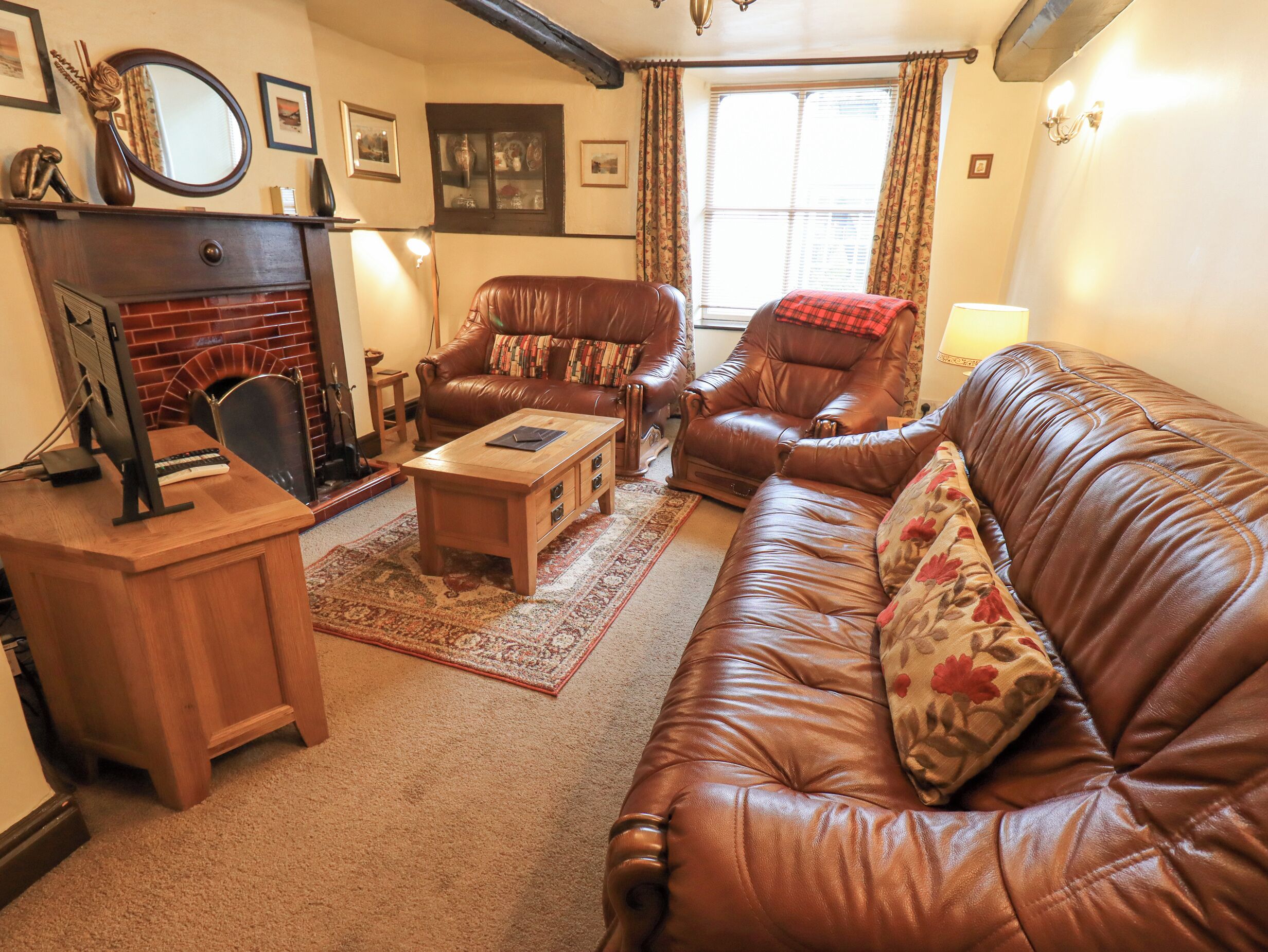 A cozy living room with a fireplace, leather sofas, a wooden coffee table, and a desk with a computer.