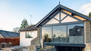 A modern house with a stone foundation, a large glass window, and a sign reading "LANDOWER". - Landower House (Ambleside)