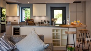 A modern kitchen with a central island, bar stools, and a seating area with a sofa and cushions. - Landower House (Ambleside)