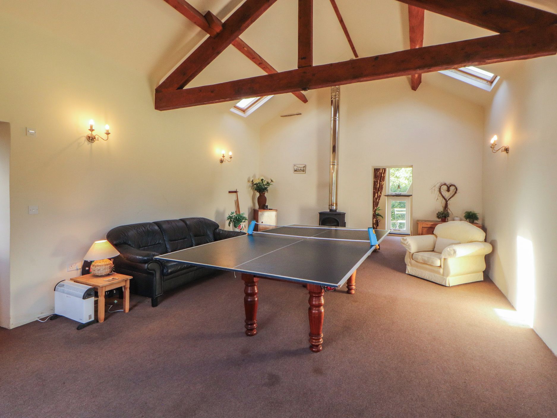 A room with a ping pong table, a sofa, a chair, and a heater.