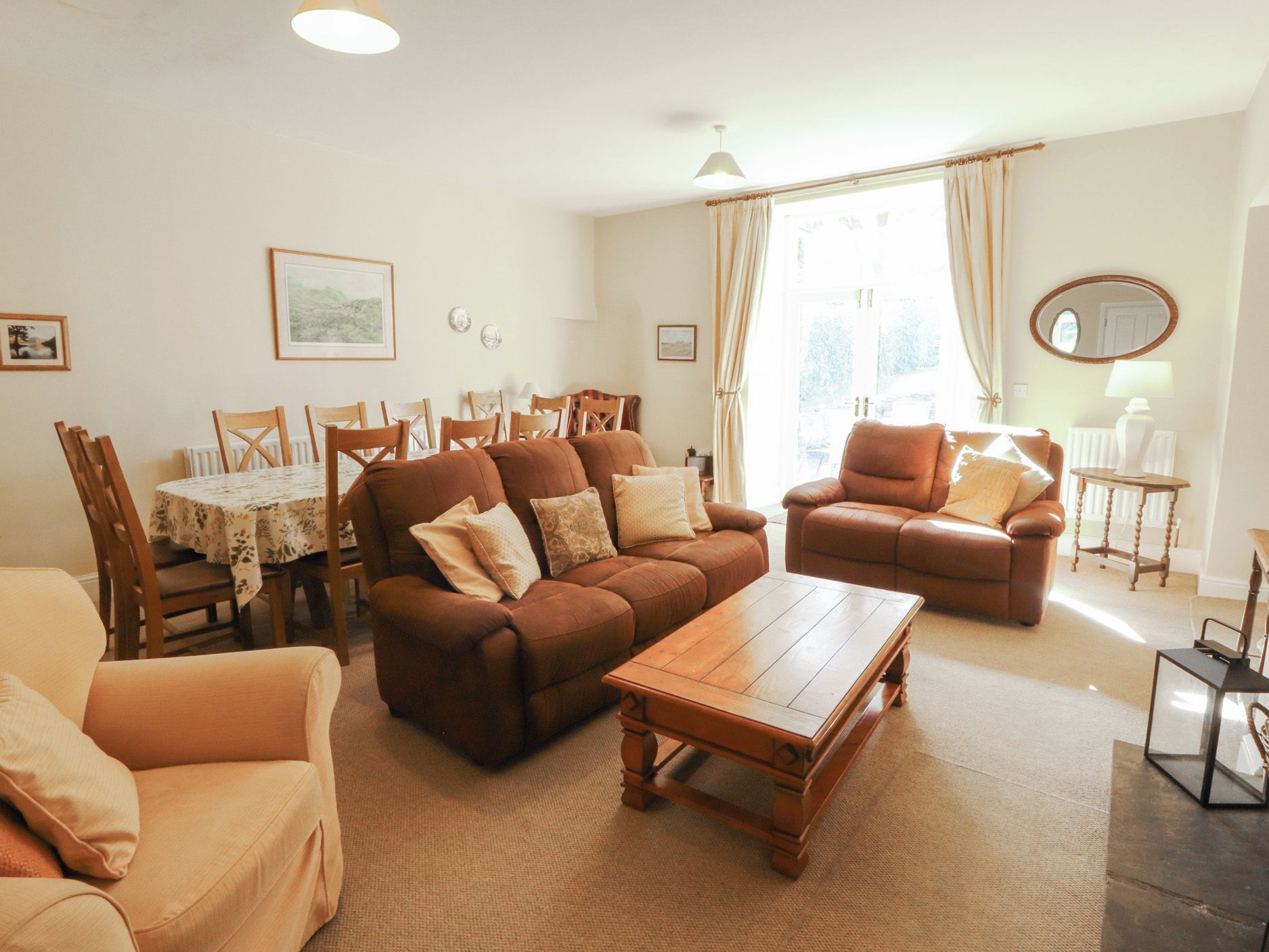 A living room with a sofa, armchair, coffee table, dining table, chairs, and a window with curtains.