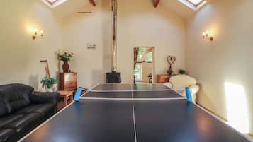 A room with a ping pong table, a fireplace, and a black leather couch.