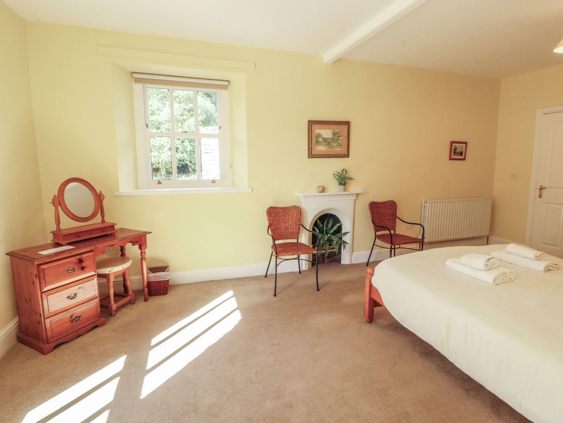 A bedroom with a bed, a dresser, a chair, a fireplace, and a window.