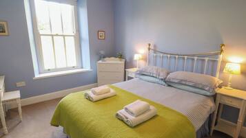A bedroom with a bed, two bedside tables, a window, and a nightstand.