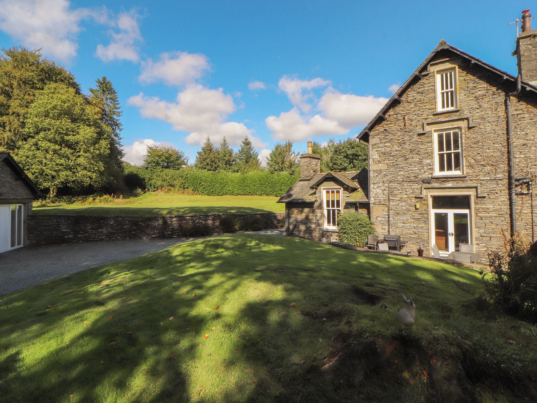 A stone house with a grassy yard, a stone wall, and a clear sky.