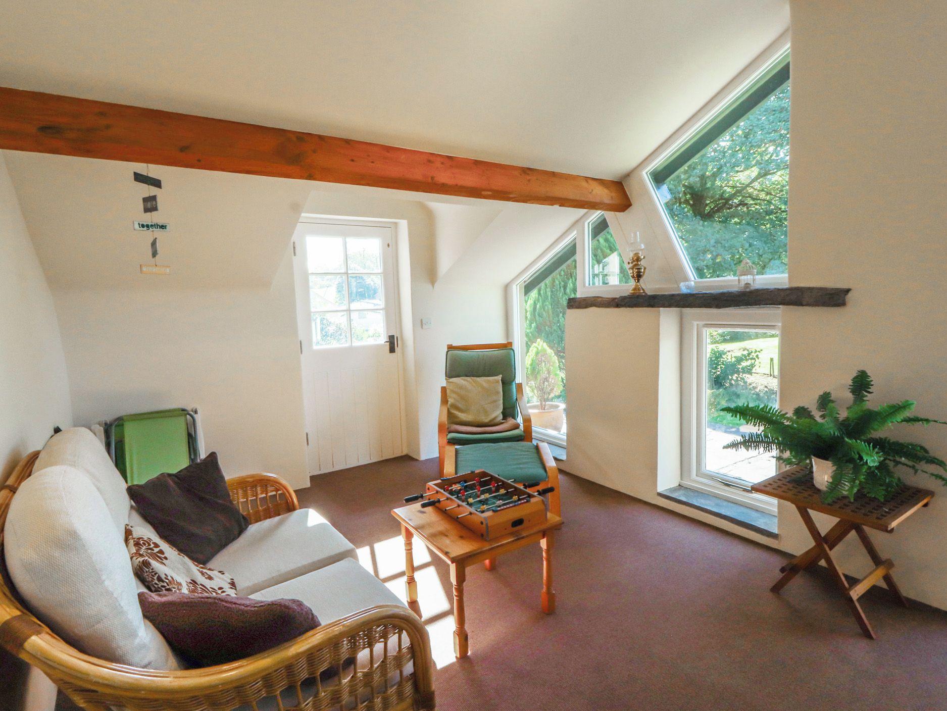 A cozy room with a sofa, a chair, a foosball table, and a potted plant.