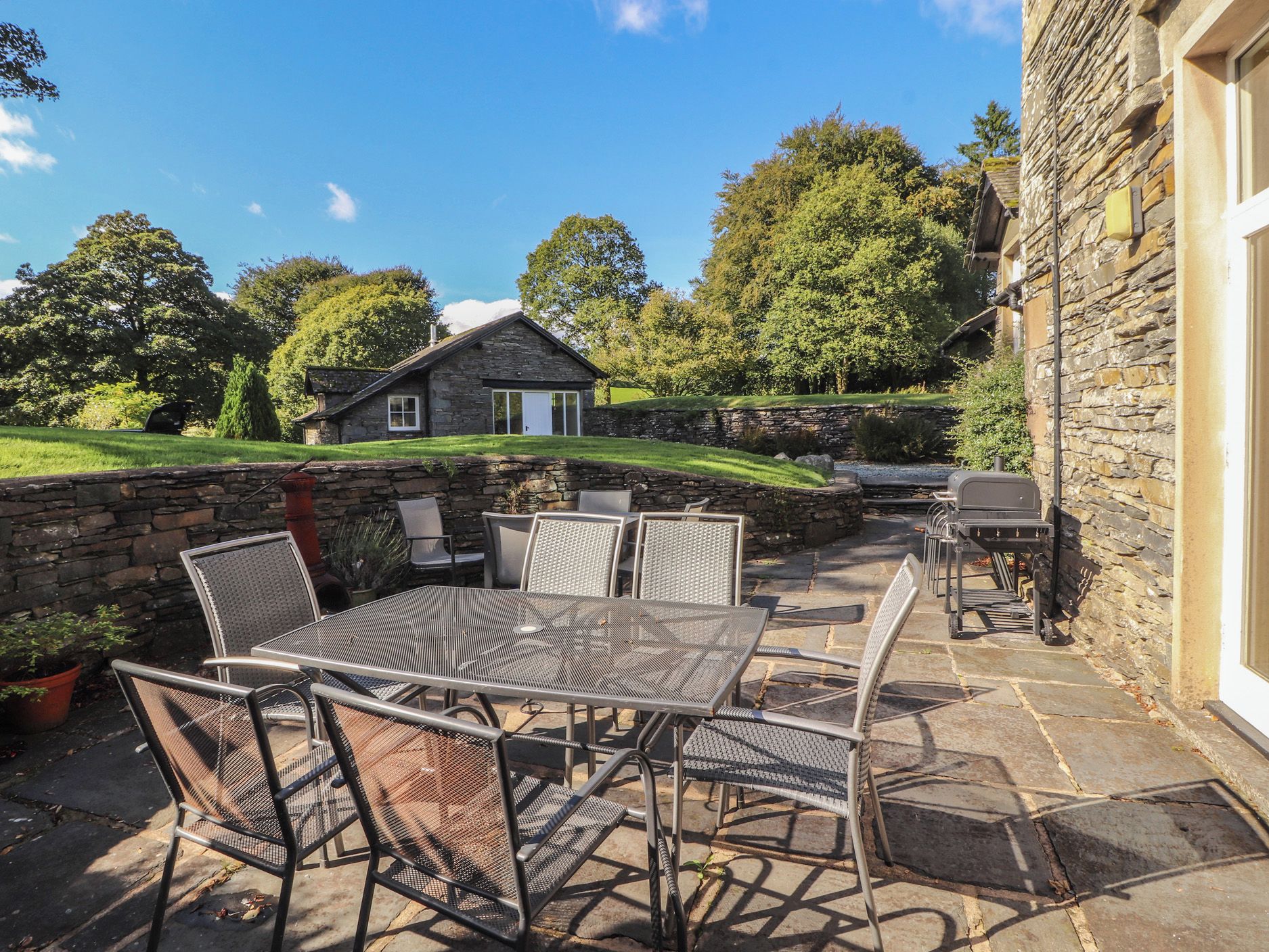 A stone building with a patio area featuring a metal table and chairs, a barbecue grill, and a stone wall.