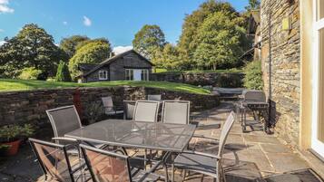 A stone building with a patio area featuring a metal table and chairs, a barbecue grill, and a stone wall.