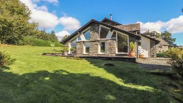 Une maison en pierre avec un toit en pente, un porche à l’avant et une pelouse bien entretenue.