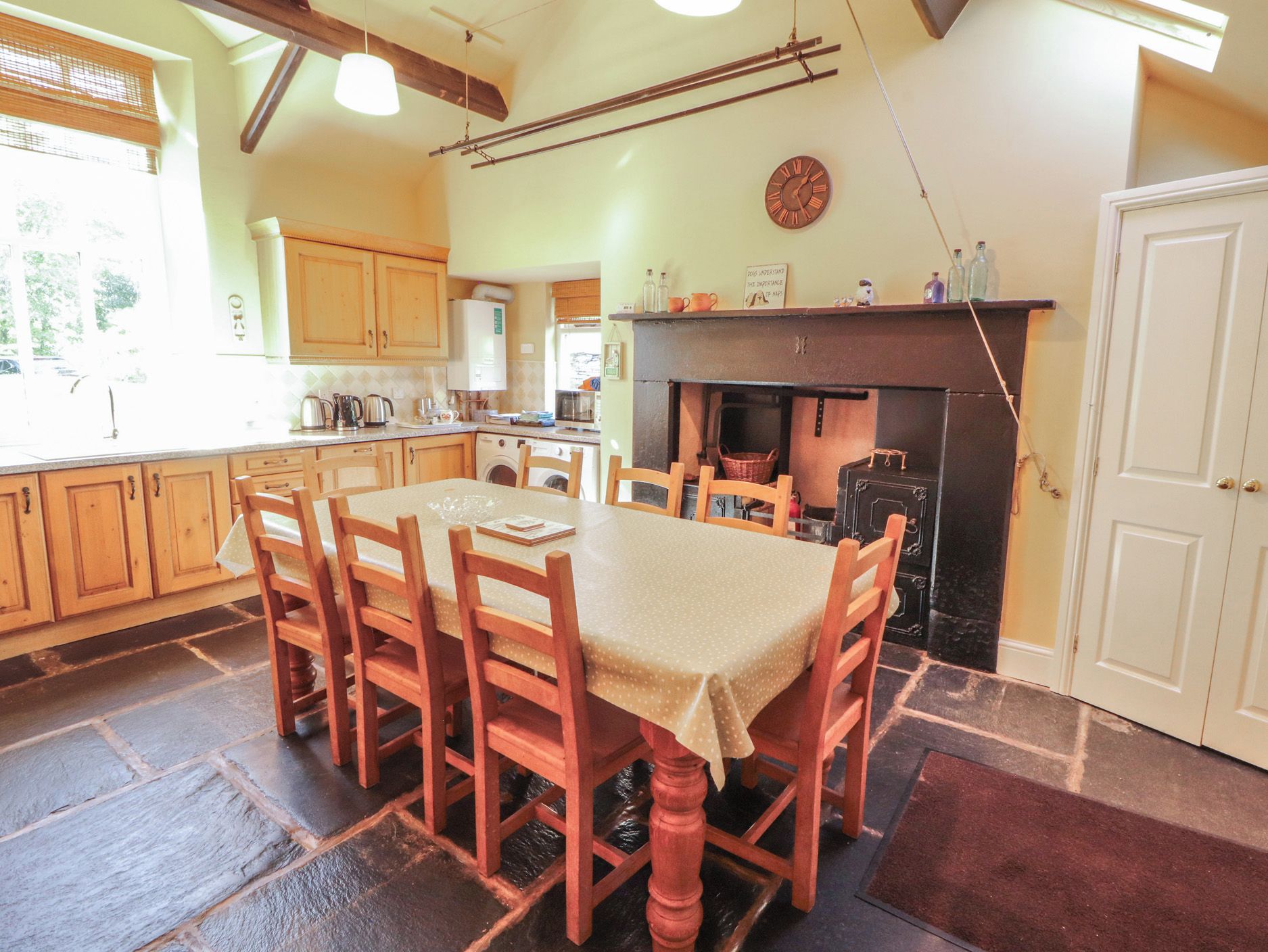 A cozy kitchen with wooden cabinets, a dining table with chairs, a fireplace, and a clock on the wall.