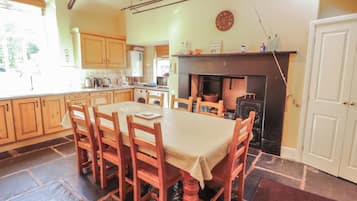 Una cocina acogedora con armarios de madera, una mesa de comedor con sillas, una chimenea y un reloj en la pared.