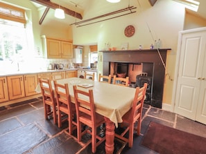 Een gezellige keuken met houten kastjes, een eettafel met stoelen, een open haard en een klok aan de muur.