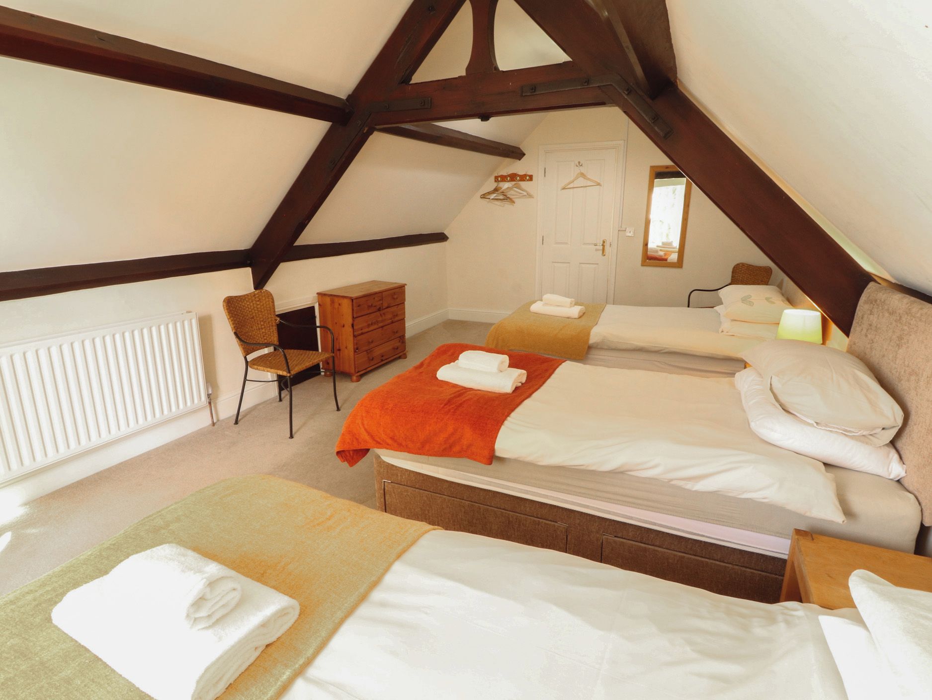 A bedroom with two beds, a chair, a dresser, and a radiator.