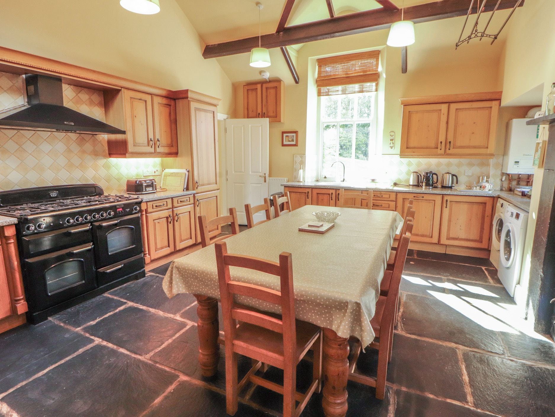 A kitchen with a dining table, wooden chairs, a stove, and a washing machine.