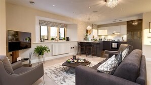 A modern living room with a sofa, coffee table, and TV. There is a kitchen area with a dining table and chairs. - Hygge at No.8 (Windermere)