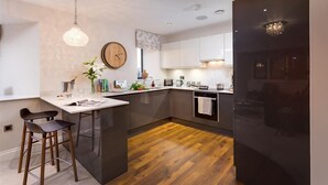 A modern kitchen with a wooden island, bar stools, a hanging light fixture, and a clock on the wall. - Hygge at No.8 (Windermere)