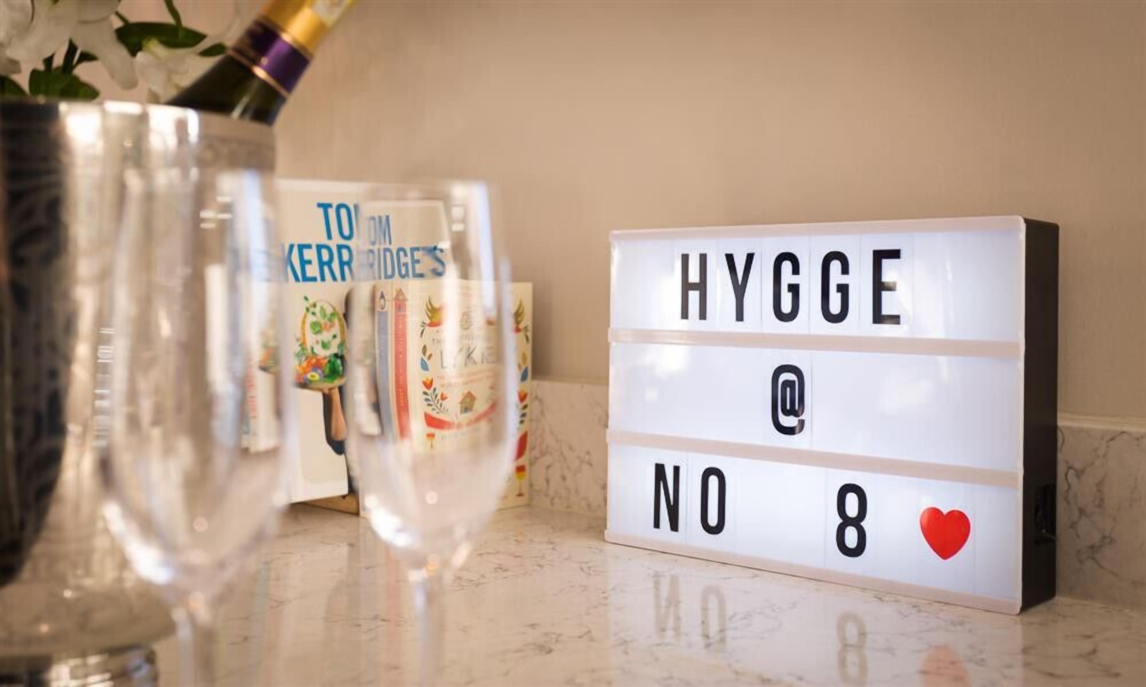 Une boîte lumineuse avec l’inscription « HYGGES @ NO 8 » et un cœur rouge, un vase en verre avec une plante, et une bouteille avec un bouchon doré.