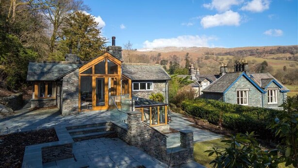A stone house with a glass conservatory, surrounded by a stone pathway and lush greenery. - Spring Cottage (Ambleside)