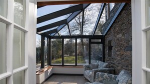 A conservatory with a stone wall, large windows, and a sofa. - Spring Cottage (Ambleside)