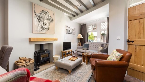 A cozy living room with a fireplace, a sofa, a television, and a large painting on the wall. - Little Leveret Cottage (Keswick)