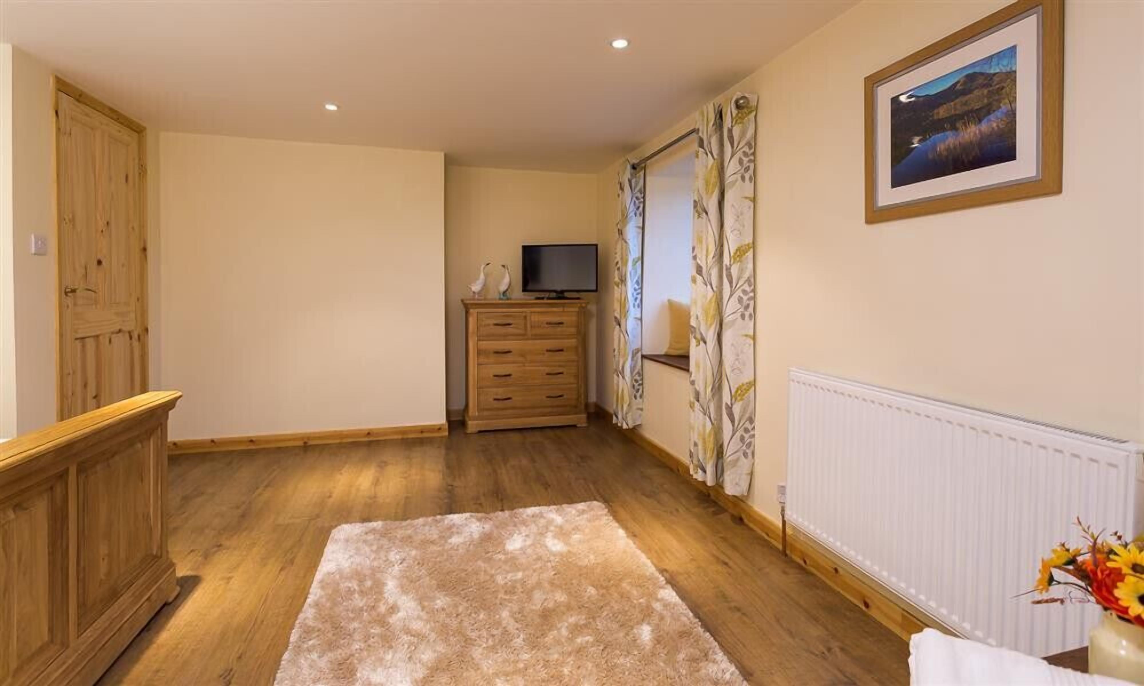 A room with wooden flooring, a wooden cabinet, a television on a stand, a radiator, and a framed picture on the wall.