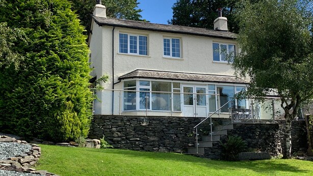 Una casa a due piani con fondamenta in pietra, una veranda in vetro e una scalinata in pietra che conduce all'ingresso.