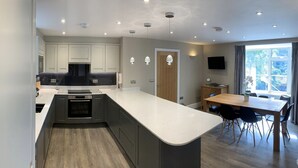Una cucina moderna con isola centrale, forno integrato e zona pranzo con tavolo e sedie in legno.