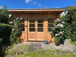 Un edificio in legno con un'ampia porta e finestre, immerso nel verde e con un vialetto sterrato.